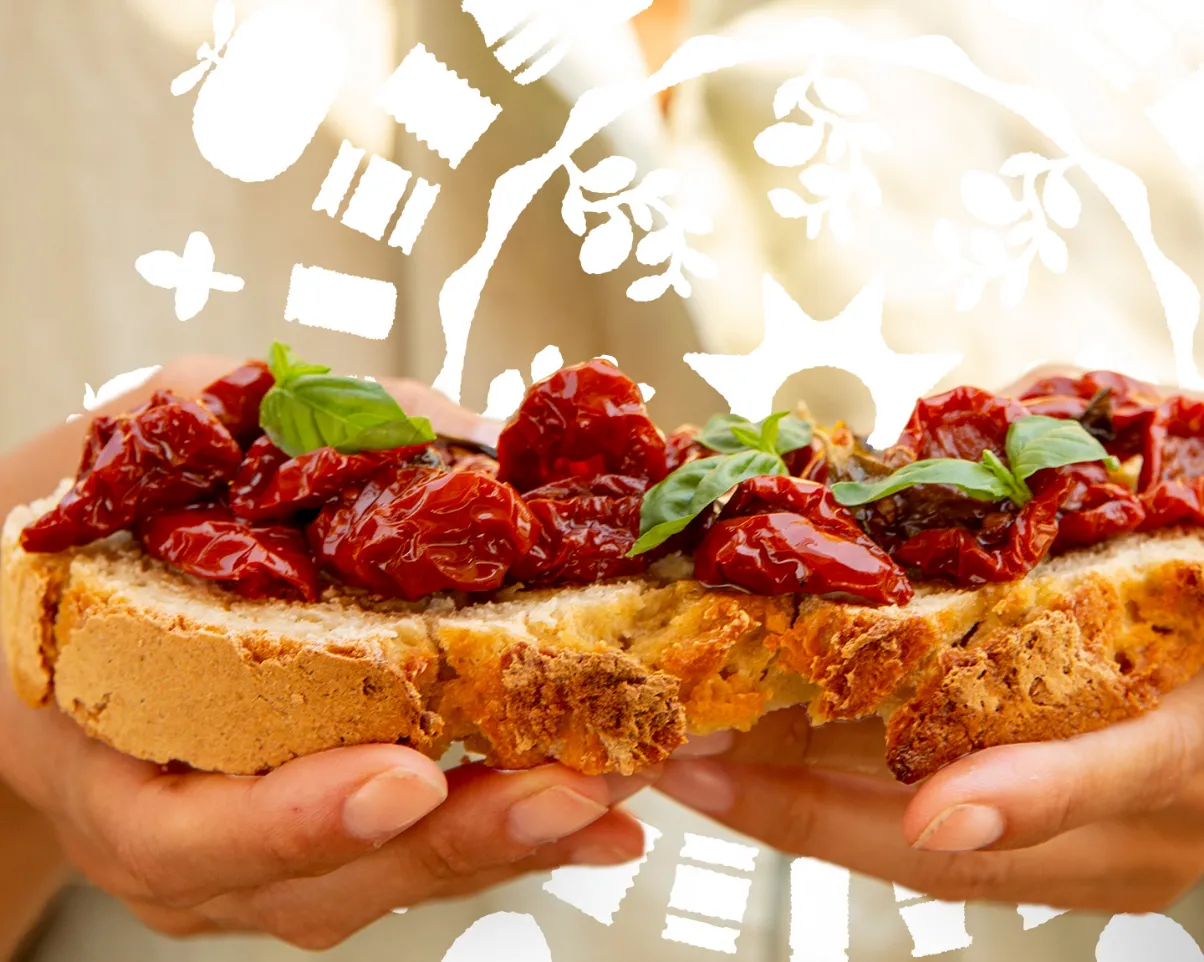 zwei Hände halten jeweils ein Bruschetta Brot reich belegt mit getrockneten Tomaten